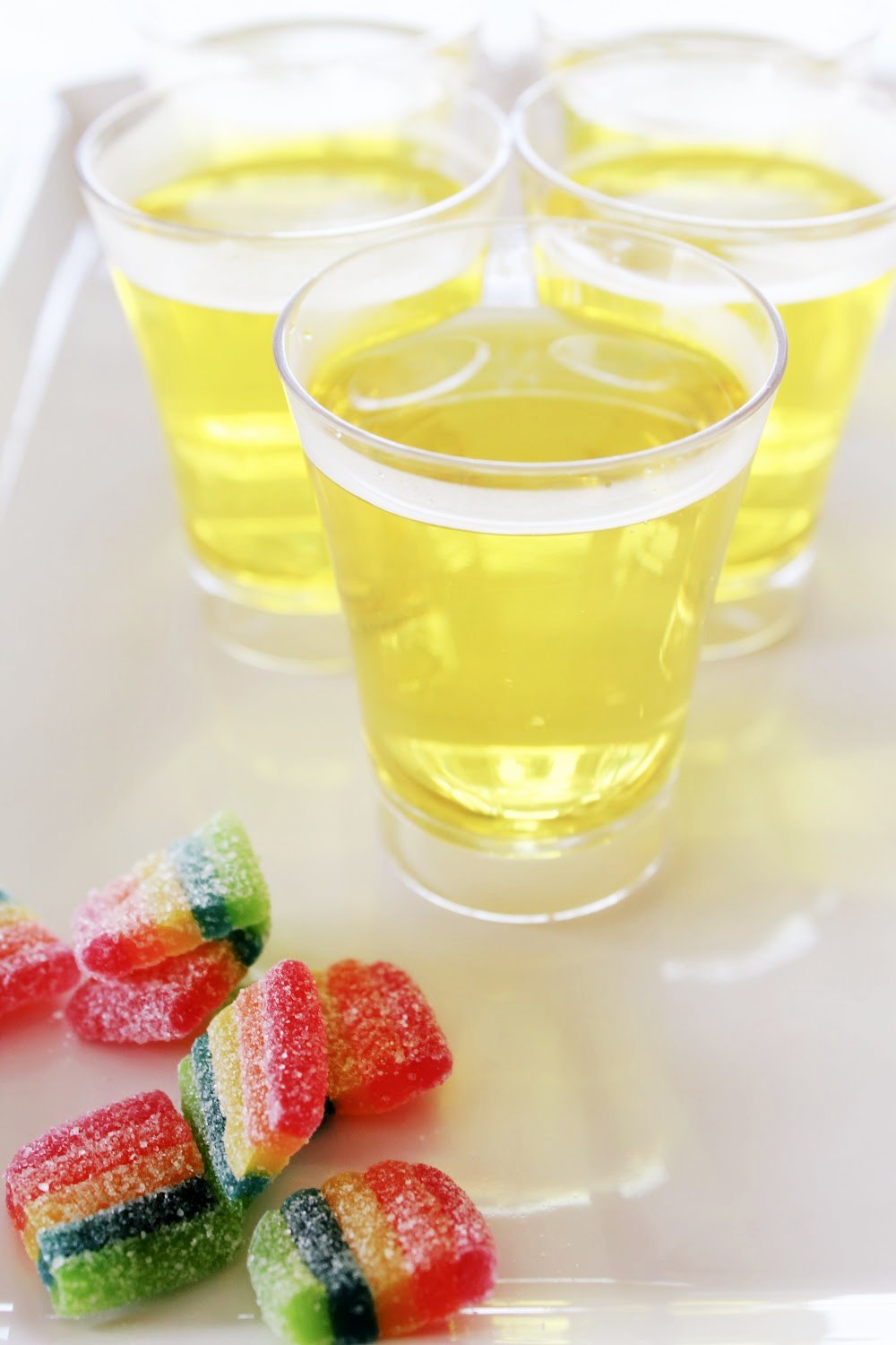 Pineapple jello shots with rainbow candy sitting beside the shot cups.