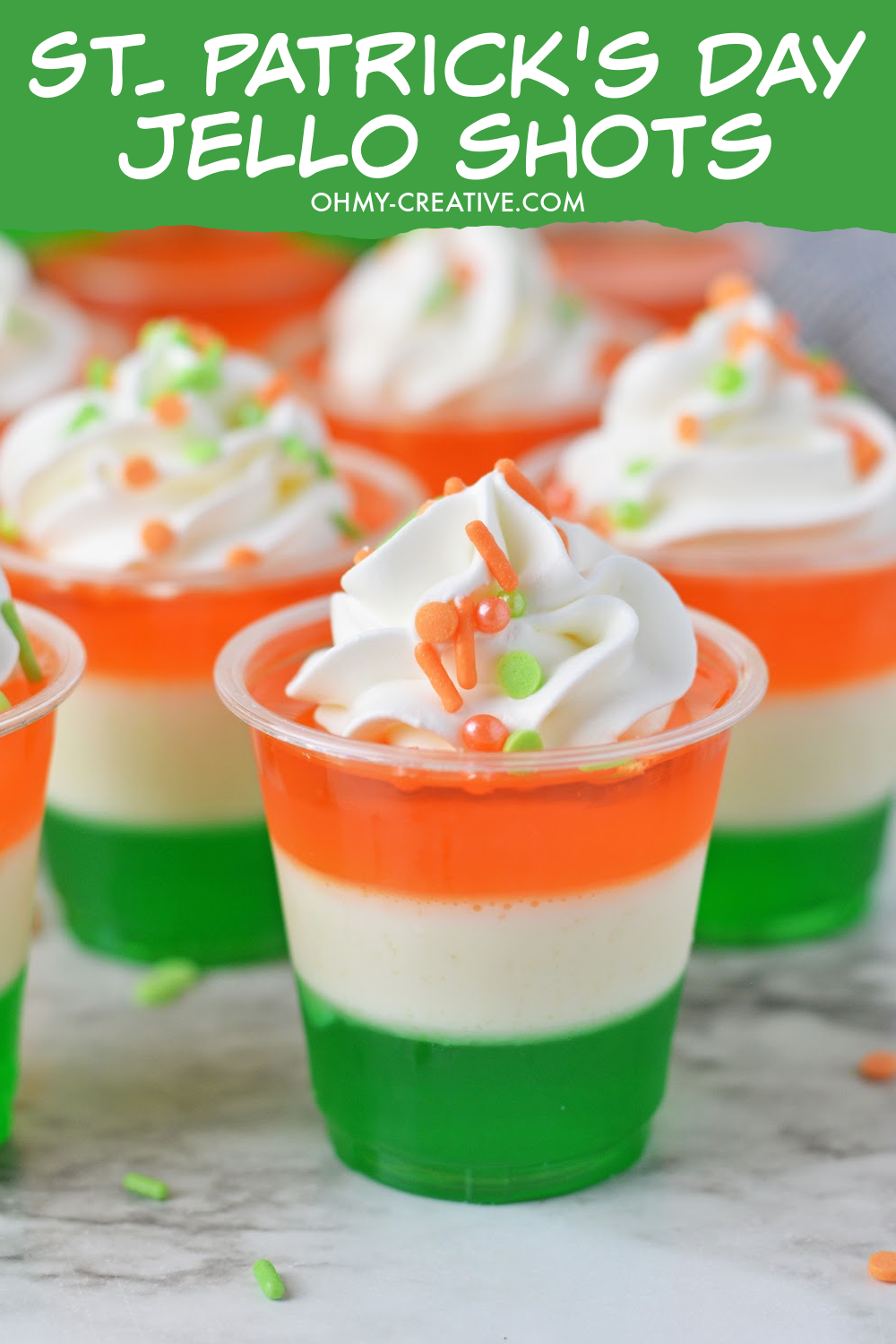 Pin image of St. Patrick's Day jello shots. Layer of green, white and orange jello topped with whipped cream.