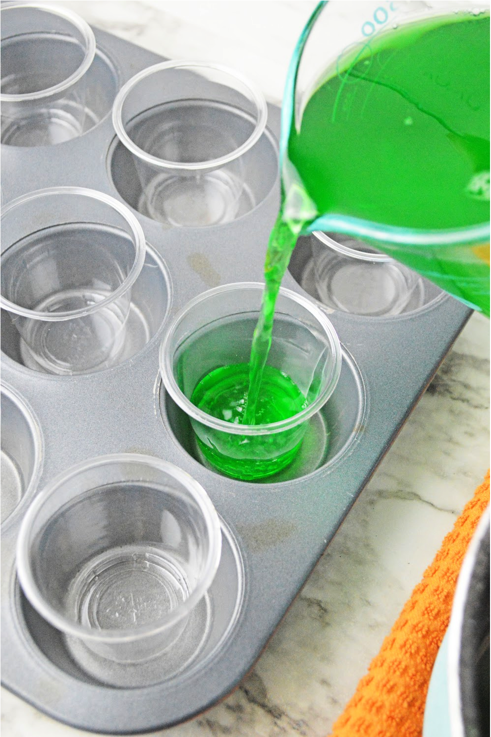Pouring green jello into shot cups in a muffin tin.