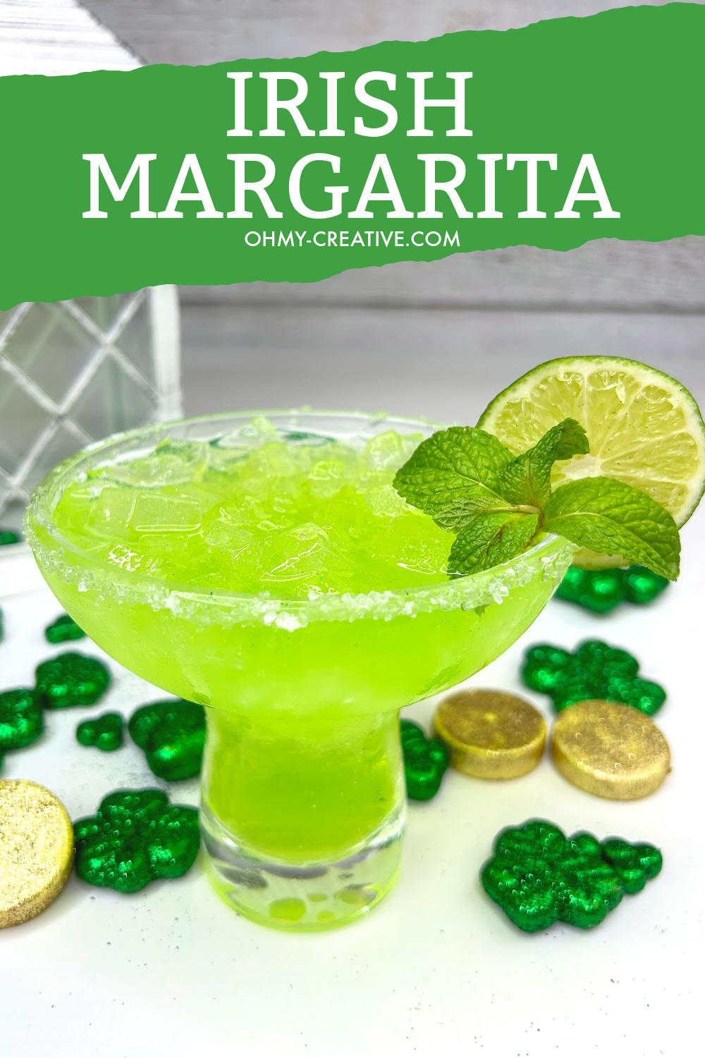 Pin image with a green Irish margarita in a margarita glass garnished with a lime. In the background are shamrocks and gold pieces.