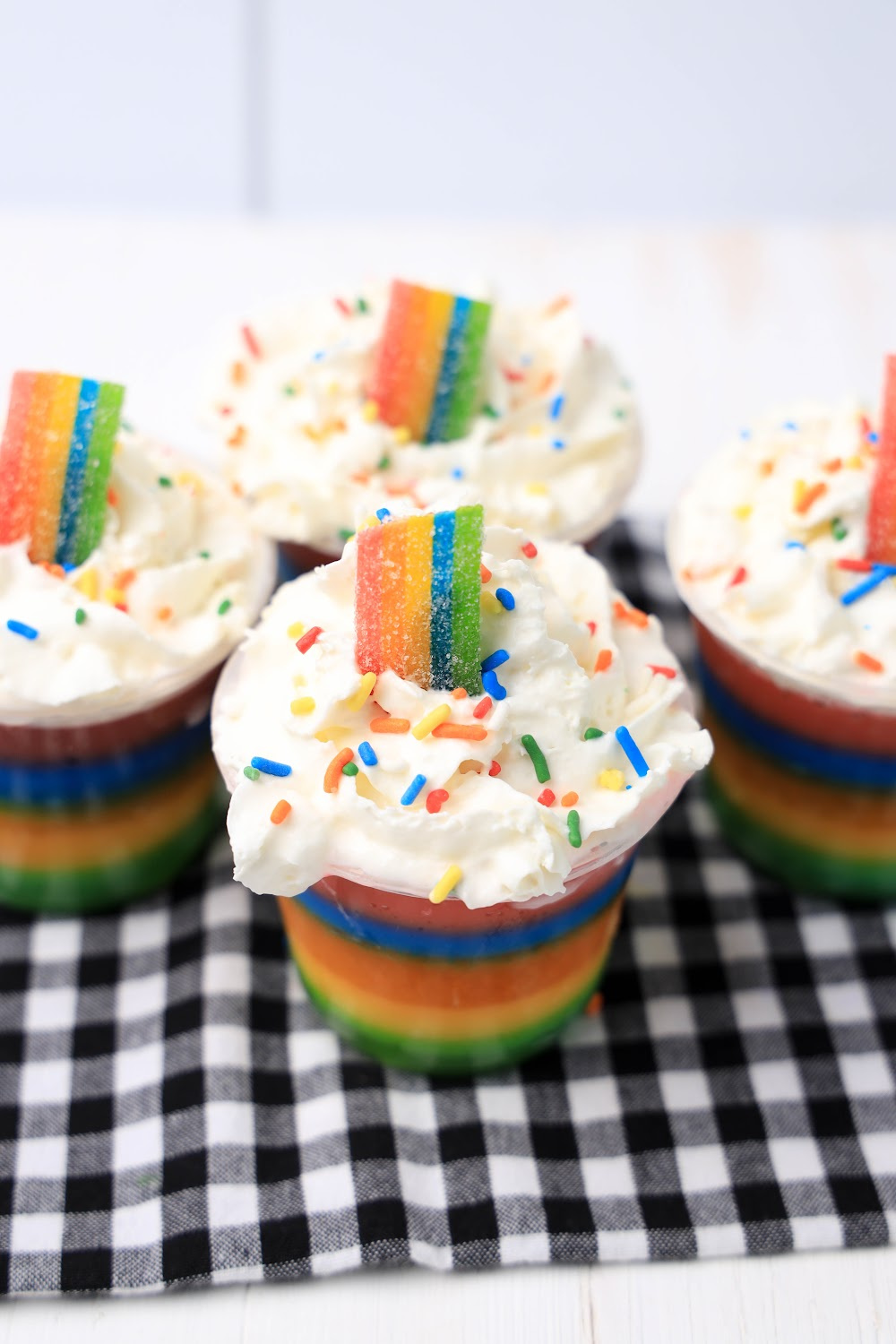 Rainbow jello shots topped with whipped cream, rainbow sprinkles and rainbow candy.