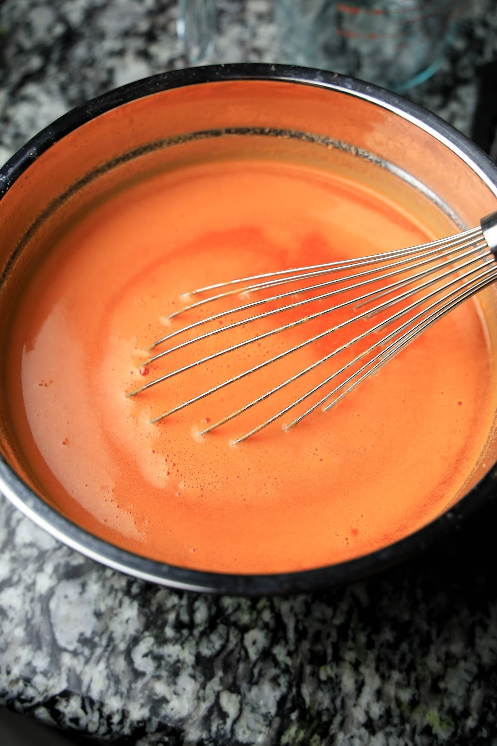 Orange jello in a sauce pan with a whisk.