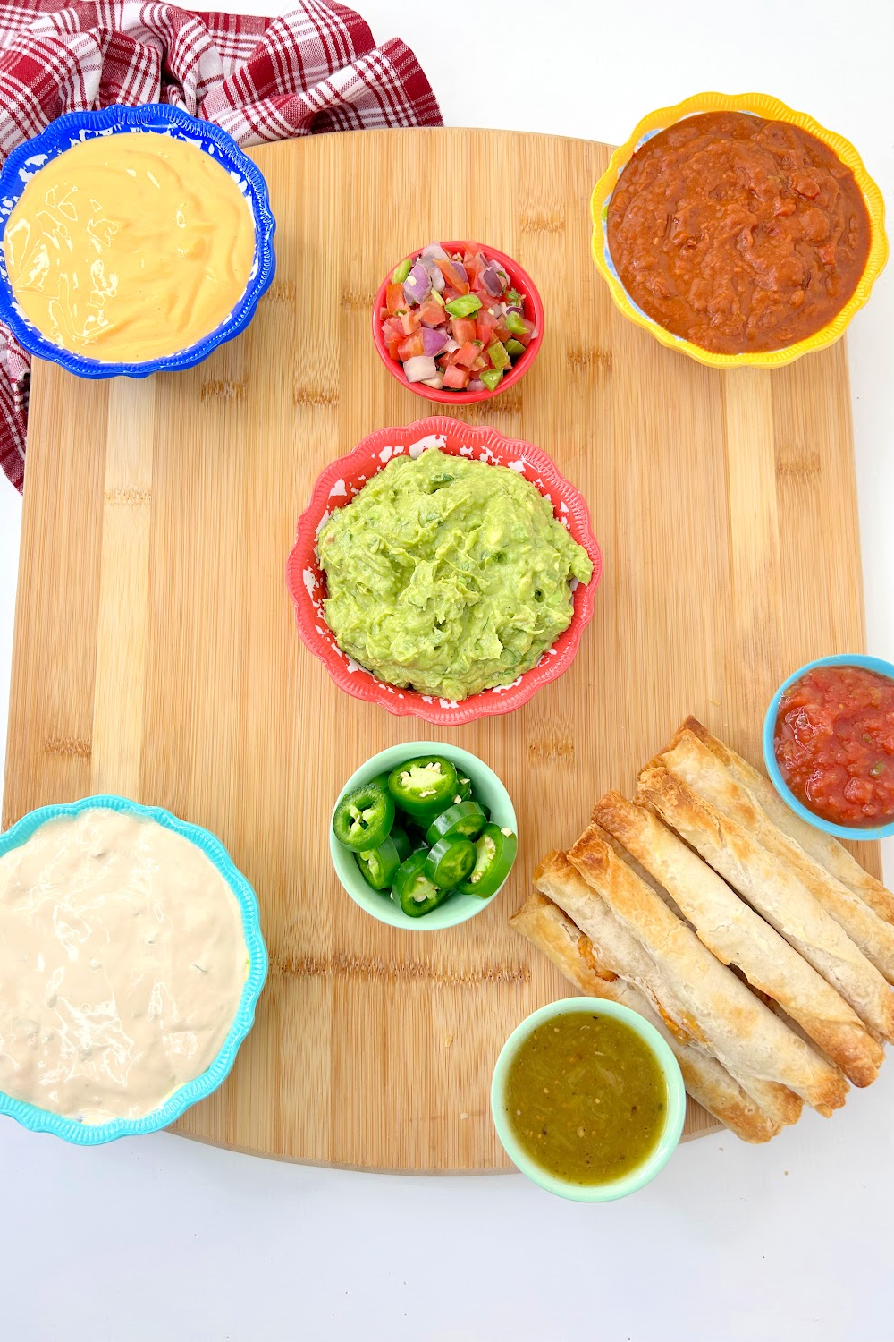 A square wooden charcuterie board with Mexican dips in the corners and smaller dips in towards the middle including a bowl of guacamole. 