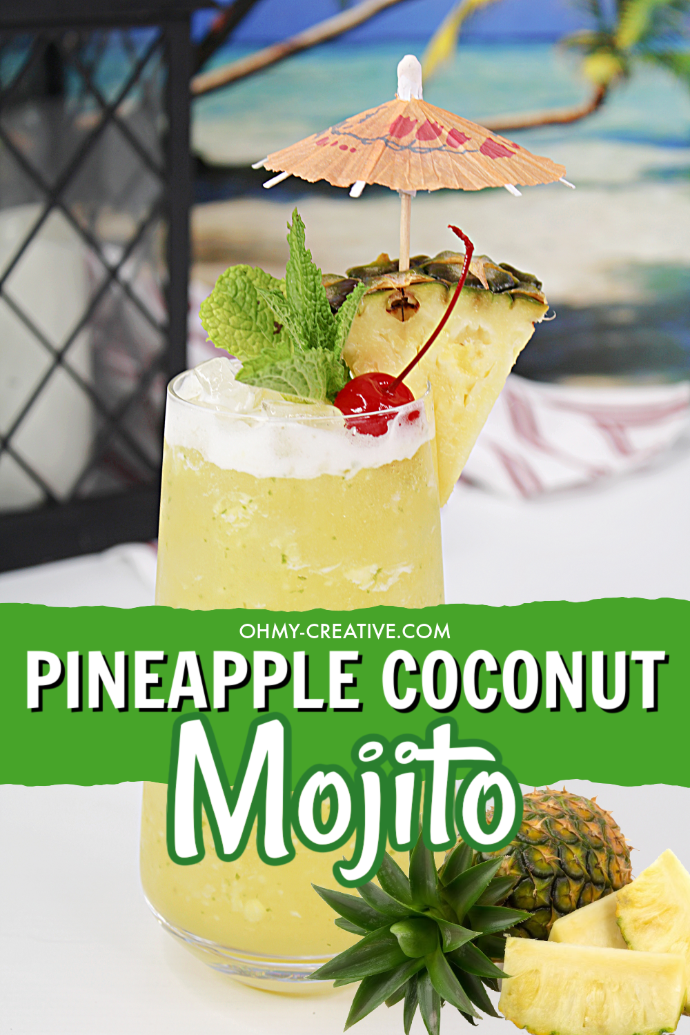 A tall glass of pineapple coconut mojito with all the flavors of the tropics! Garnished with a wedge of pineapple, maraschino cherry and an umbrella. A tropical beach scene is in the background.
