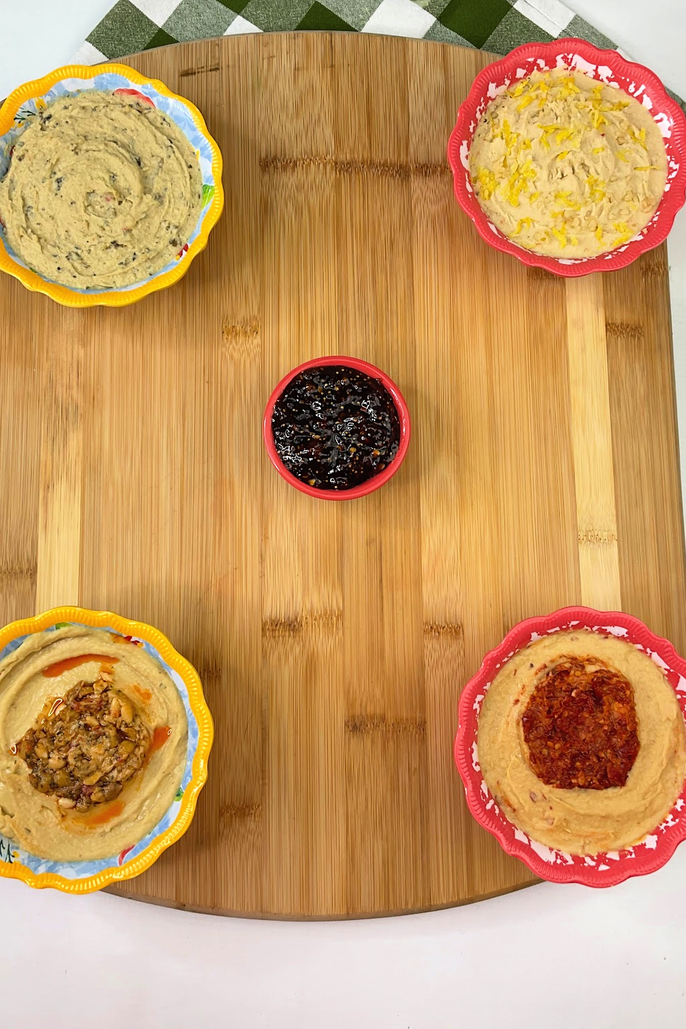 Building a charcuterie board with bowls of hummus dips in the corners of the board. 