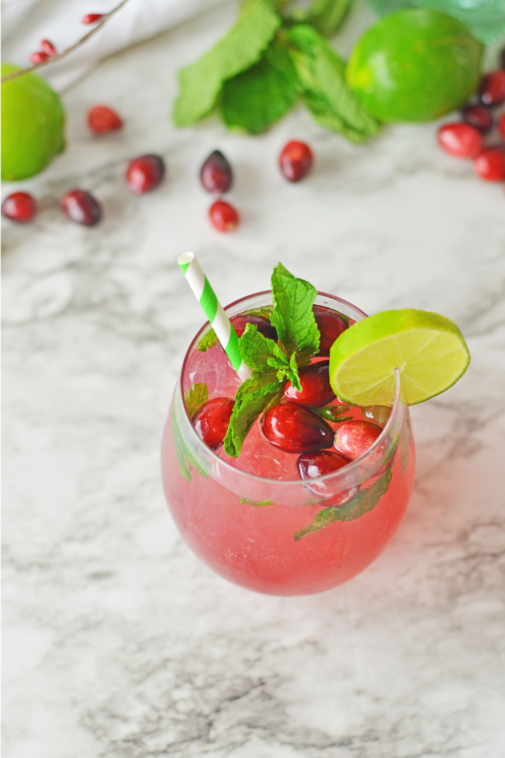 a view of a cranberry mojito from above. Cranberries and limes can be seen in the background.