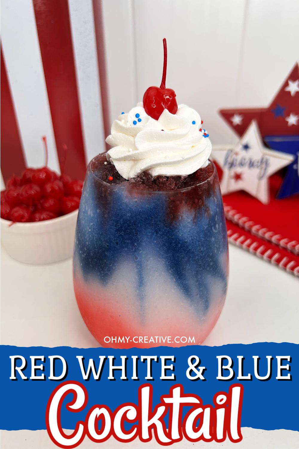 Featuring festive, patriotic colors, this Red White, And Blue Cocktail is like frozen slushy with red on the bottom and blue on the top layer with whipped cream and a cherry on top. Added are patriotic sprinkles. A bowl of extra cherries are off to the side and wooden star decorations in the background.