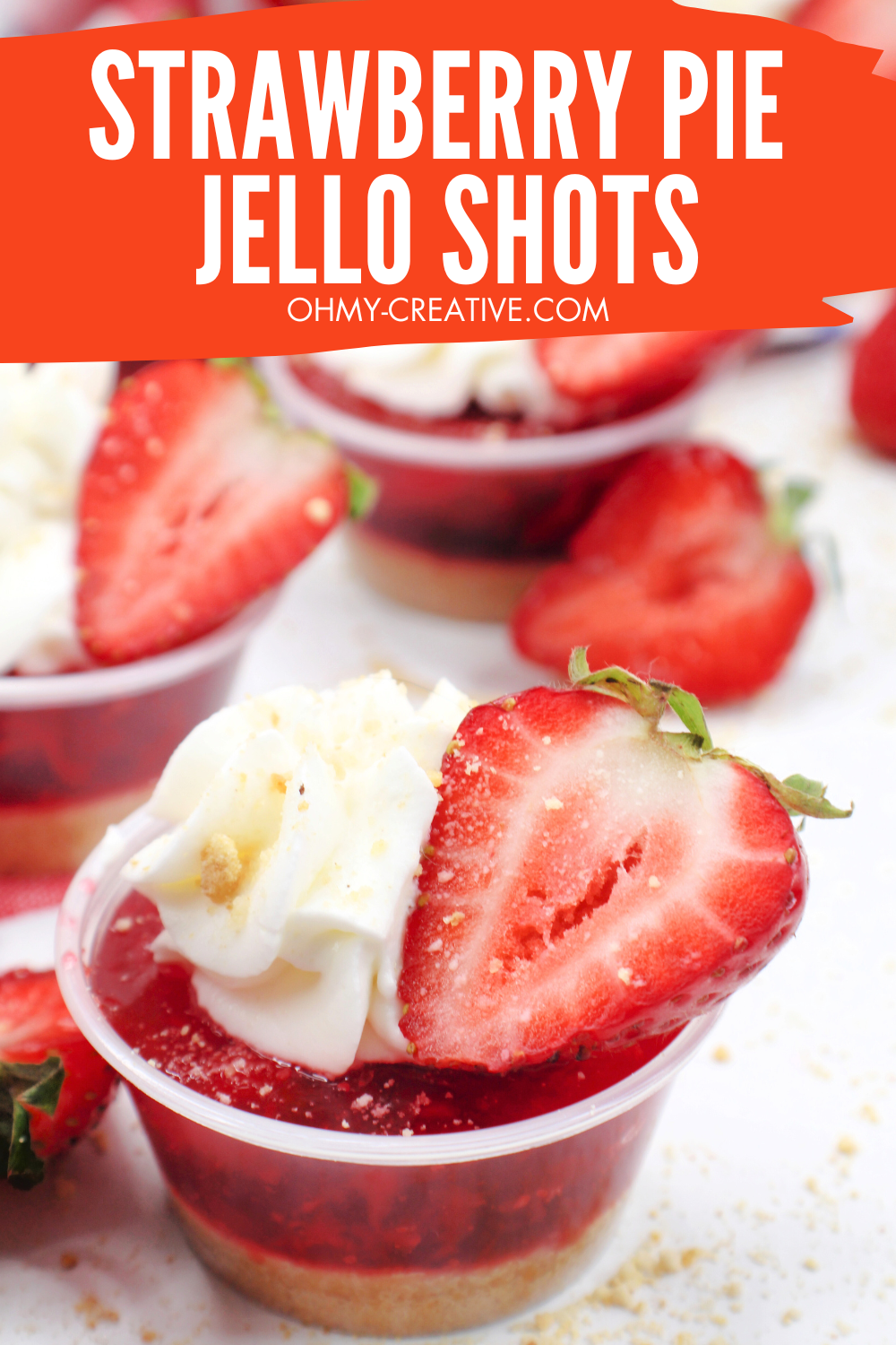 A tasty strawberry jello shot topped with whipped cream and a slice of strawberry.
