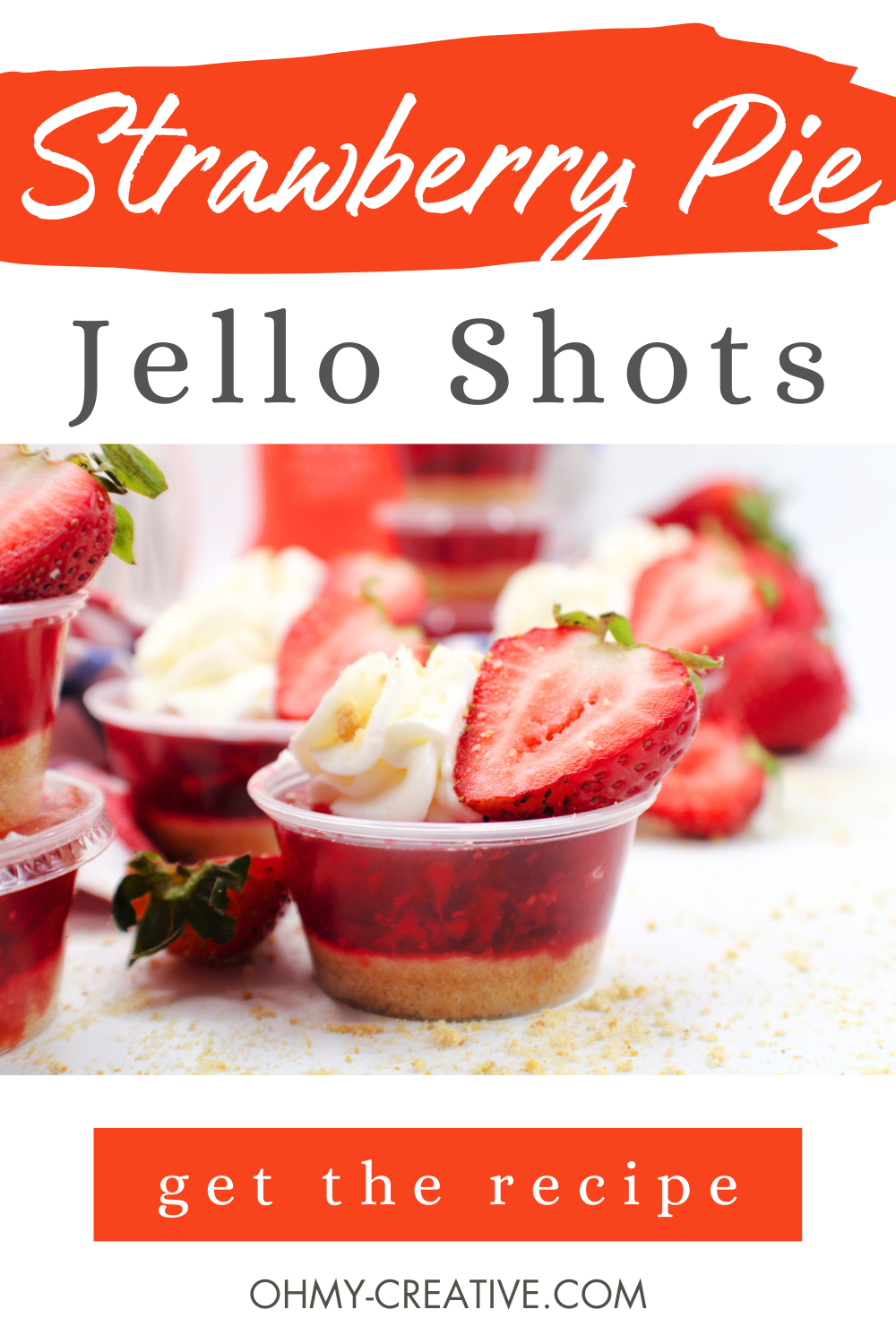 A tasty strawberry jello shot topped with whipped cream and a slice of strawberry. Fresh strawberries are in the background.