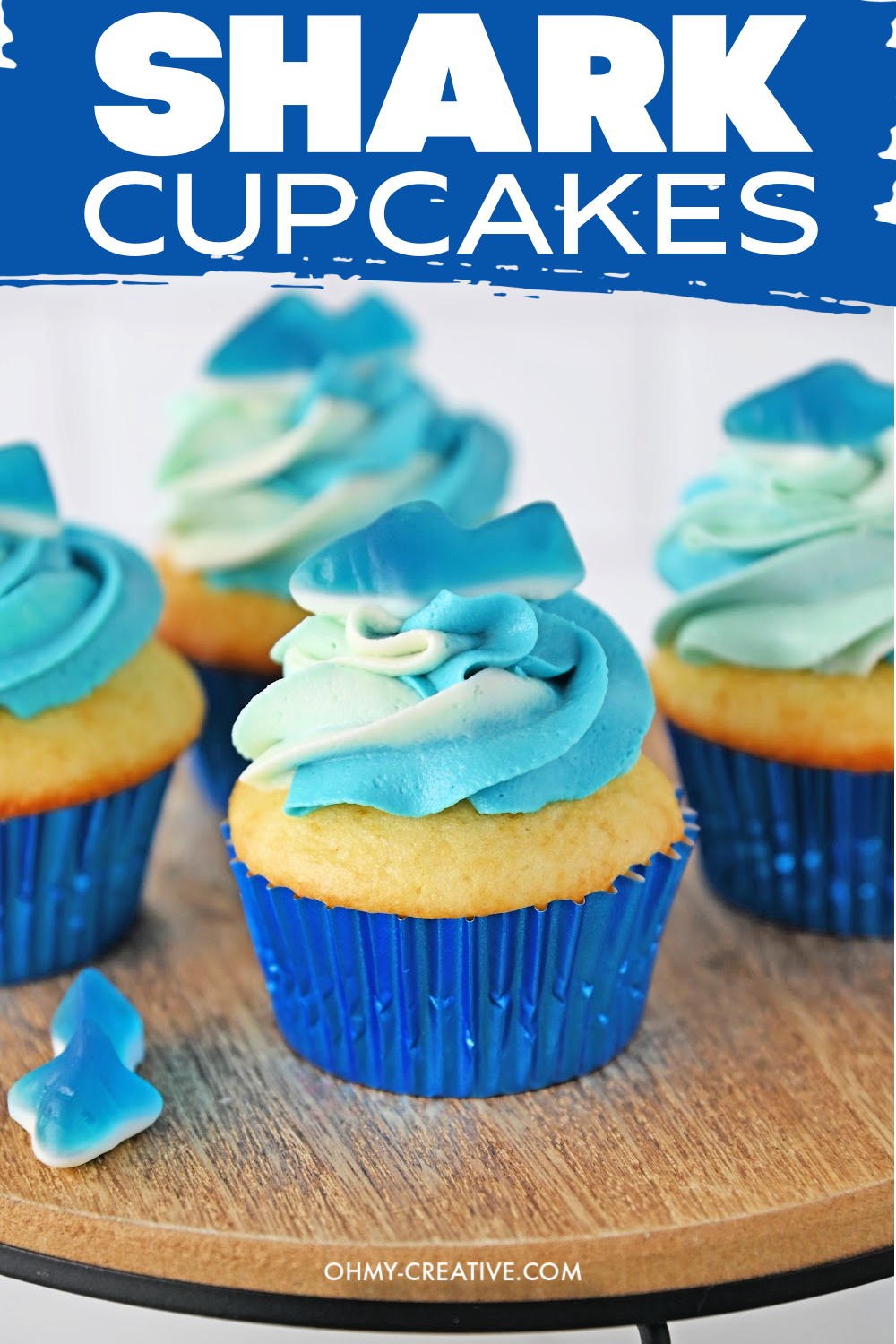Pinterest image of shark cupcakes using blue ombre icing and a gummy shark on top.