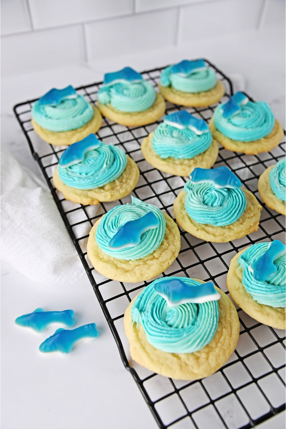 Shark cookies on a baking cooling rack with blue icing and a gummy shark.
