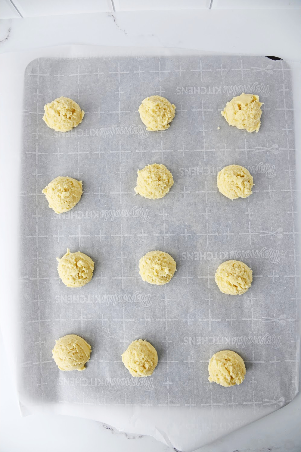 raw sugar cookie dough balls on a baking sheet lined with parchment paper.