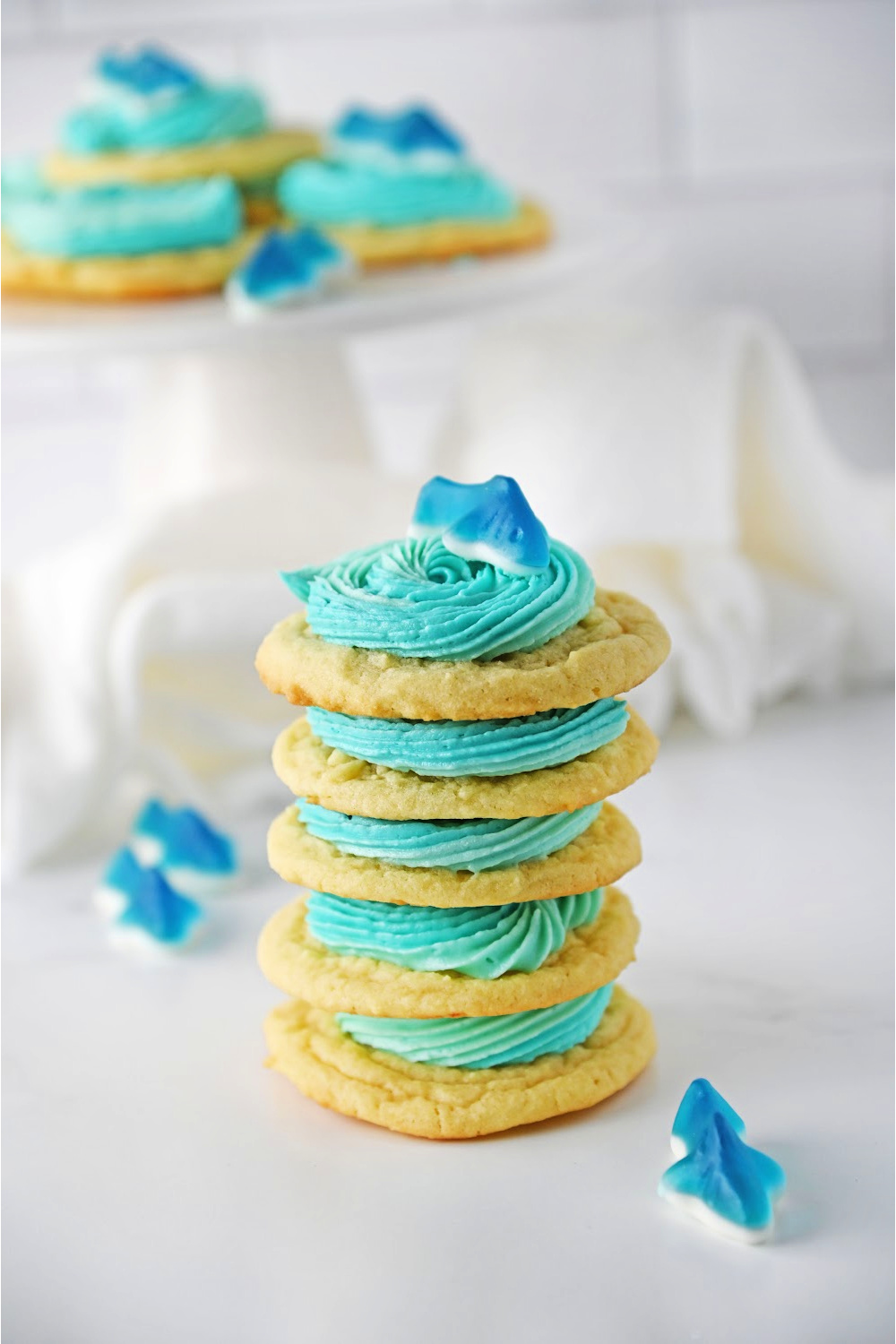 Stacked Shark cookies on a white background with blue icing and a gummy shark.