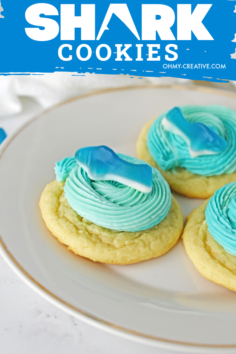 Shark cookies on a white plate with blue icing and a gummy shark.