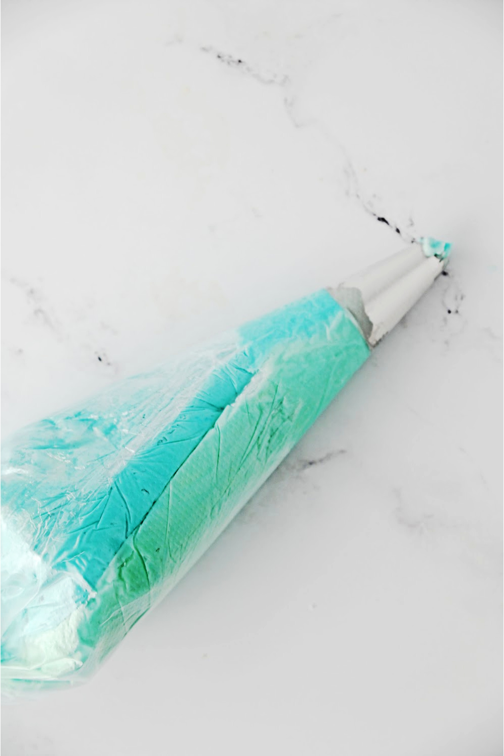 blue and light green icing wrapped individually in plastic wrapped and placed in an icing bag with a star tip.