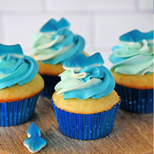 DIY shark cupcakes using blue ombre icing and a gummy shark on top sitting on a wood serving tray