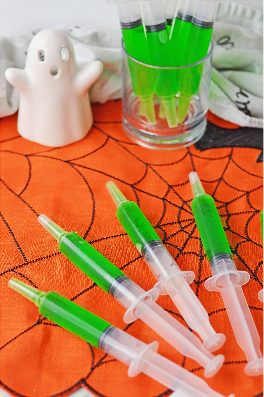 Green syringe jello shots laying on an orange spiderweb placemat.