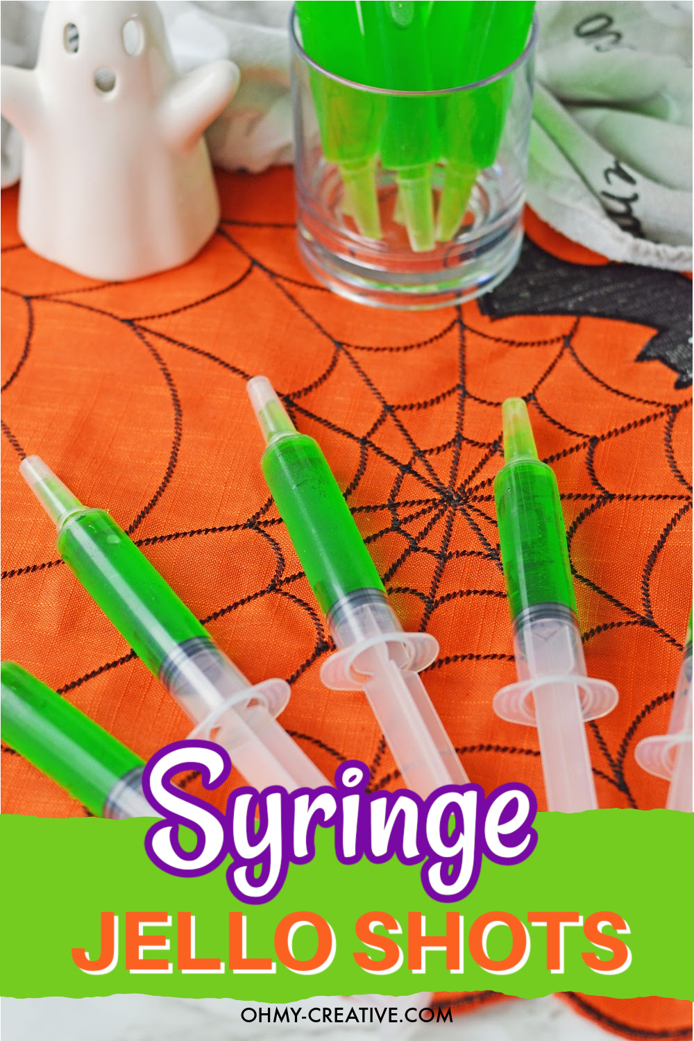 Green syringe jello shots laying on an orange spiderweb placemat.