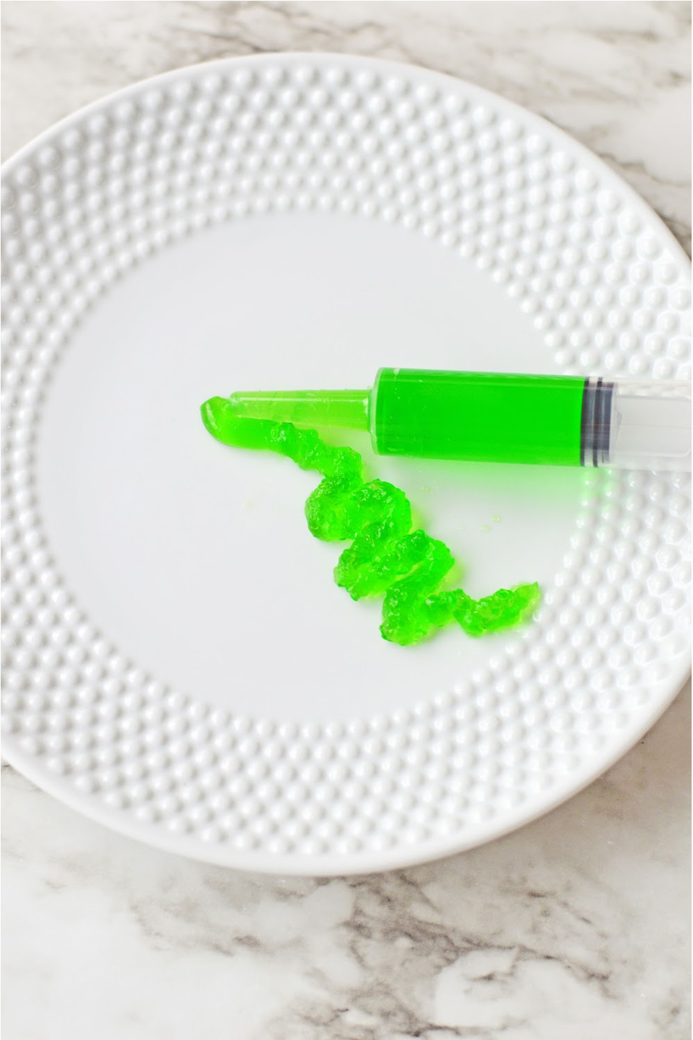green jello being squeezed out of a syringe onto a white plate.