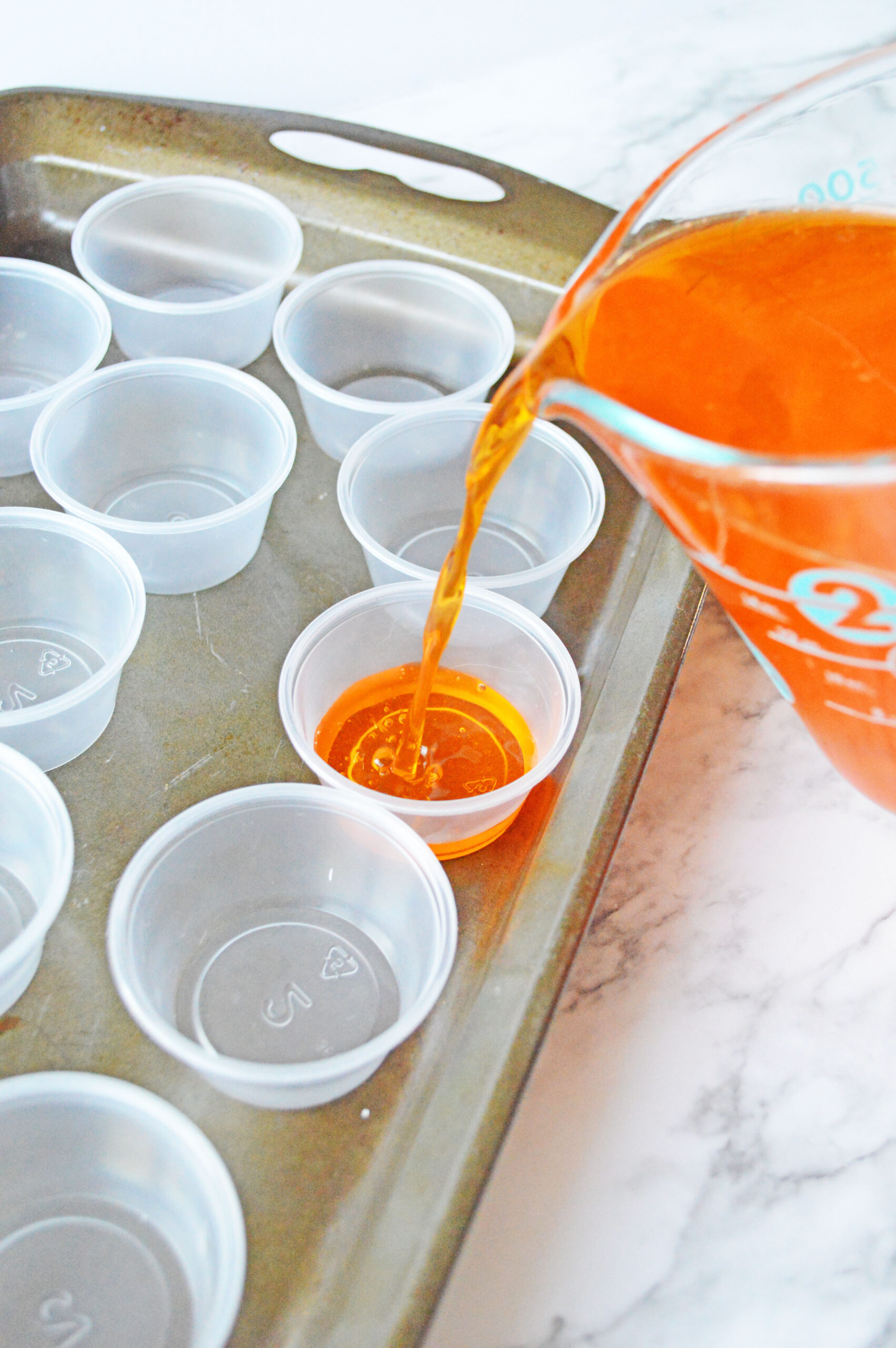 Pouring the creamcicle jello shot liquid into plastic shot cups 