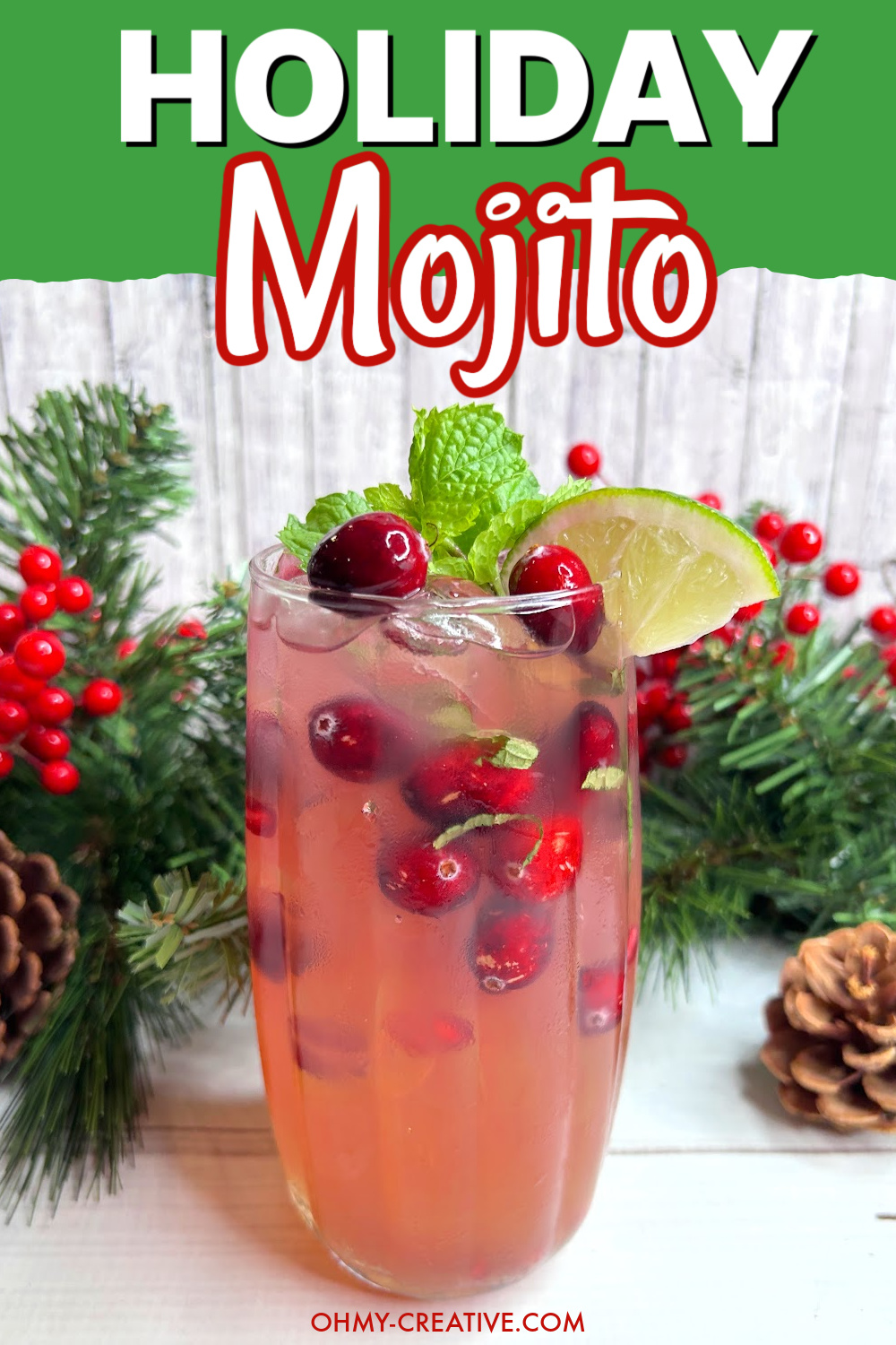 A pinterest image with a holiday mojito garnished with cranberries, mint and a wedge of lime. Winter greens are seen in the background.
