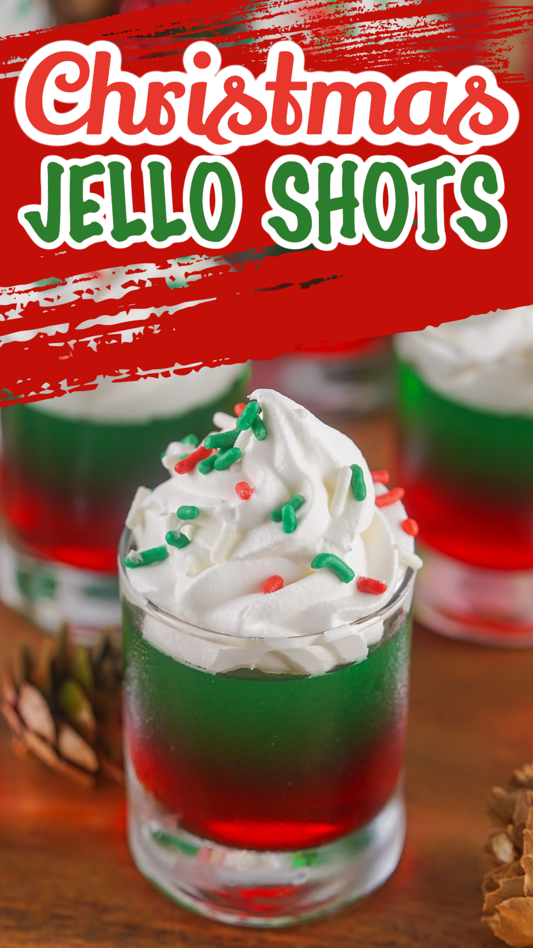 red and green layered Christmas jello shots topped with wiped cream and Christmas sprinkles.