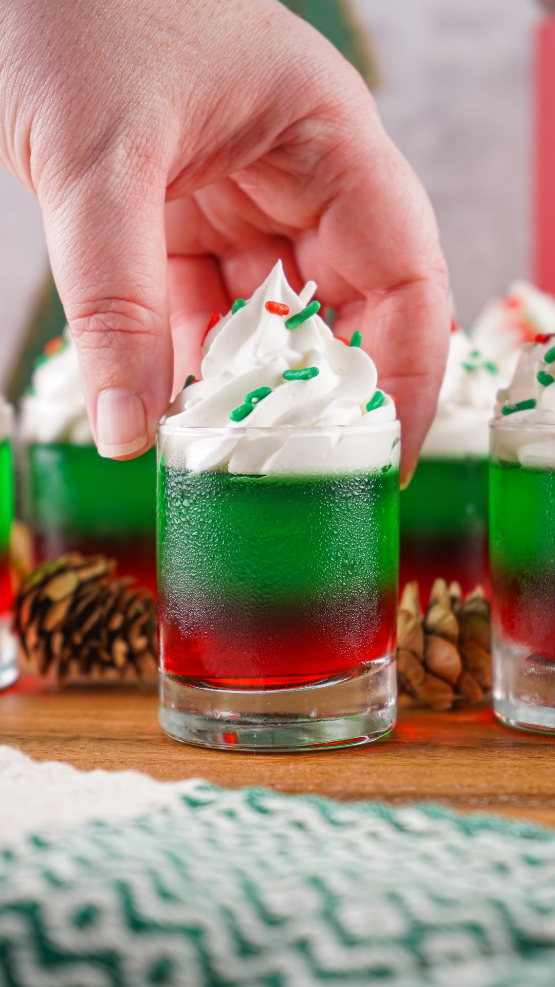 red and green layered Christmas jello shots topped with whipped cream and Christmas sprinkles.