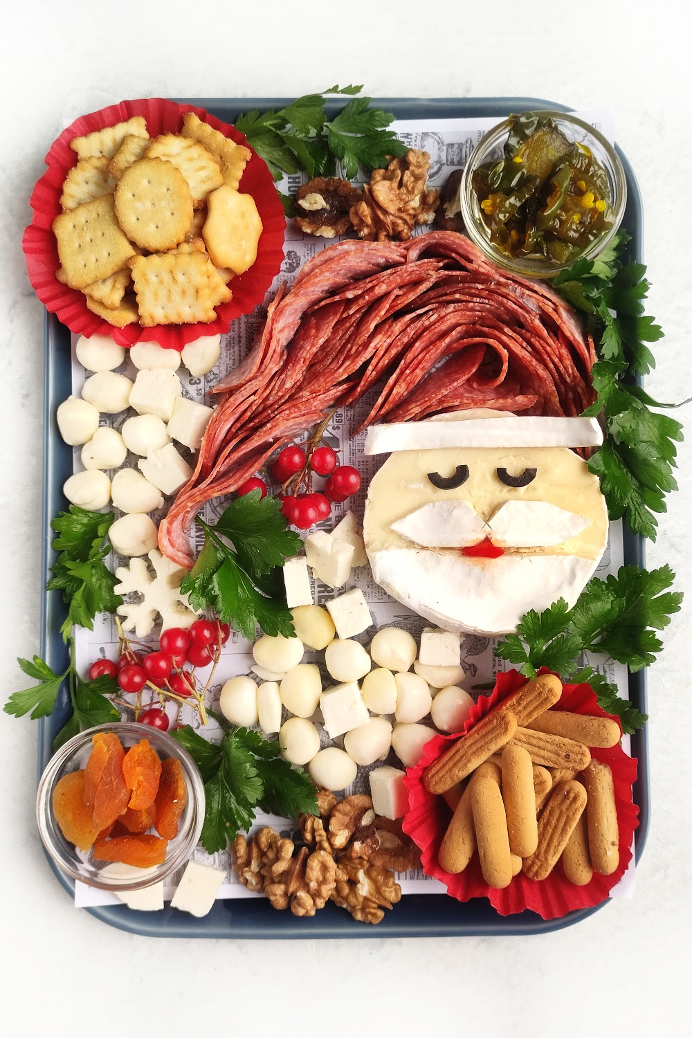 Santa Charcuterie Board. Santa is made out of brie cheese with a salami Santa hat. The Santa cheese is surrounded by other cheeses, crackers, dried fruit and nuts.