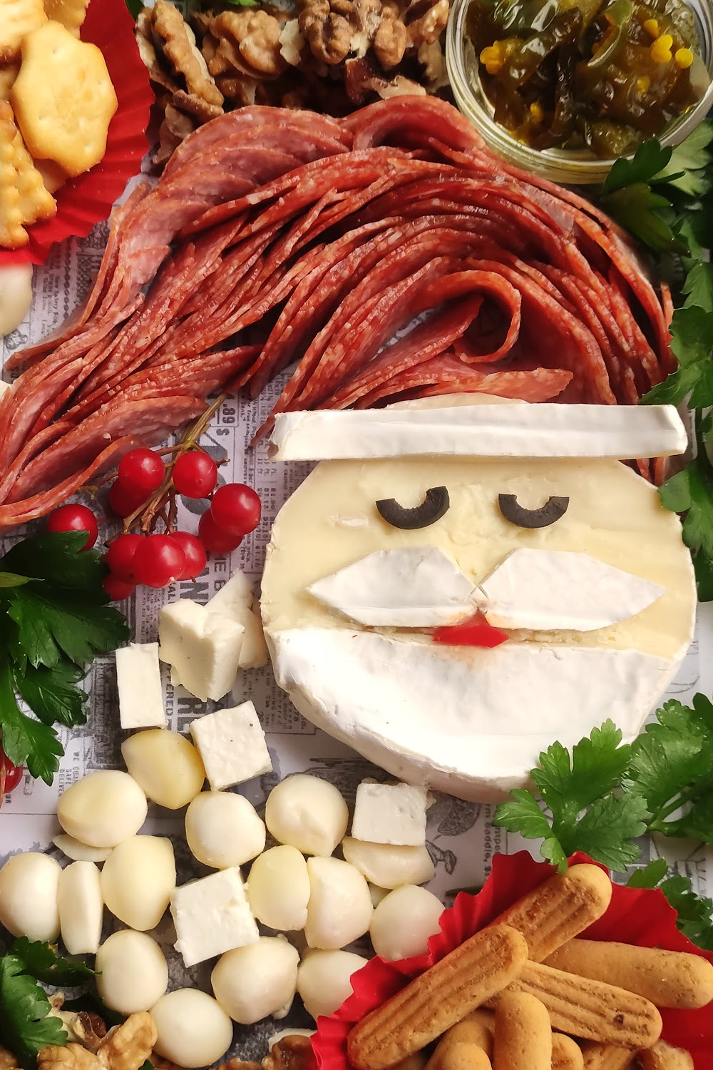Santa Charcuterie Board. Santa is made out of brie cheese with a salami Santa hat. The Santa cheese is surrounded by other cheeses, crackers, dried fruit and nuts.