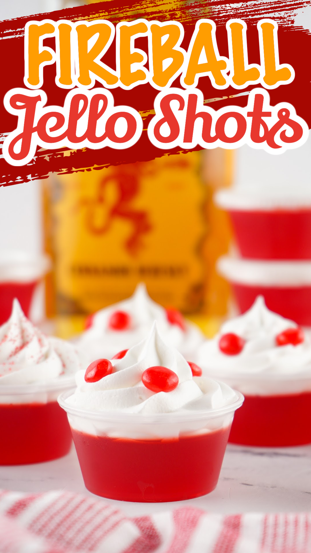 Red fireball jello shots with a bottle of Fireball in the background. Topped with whipped cream and red hot candy.