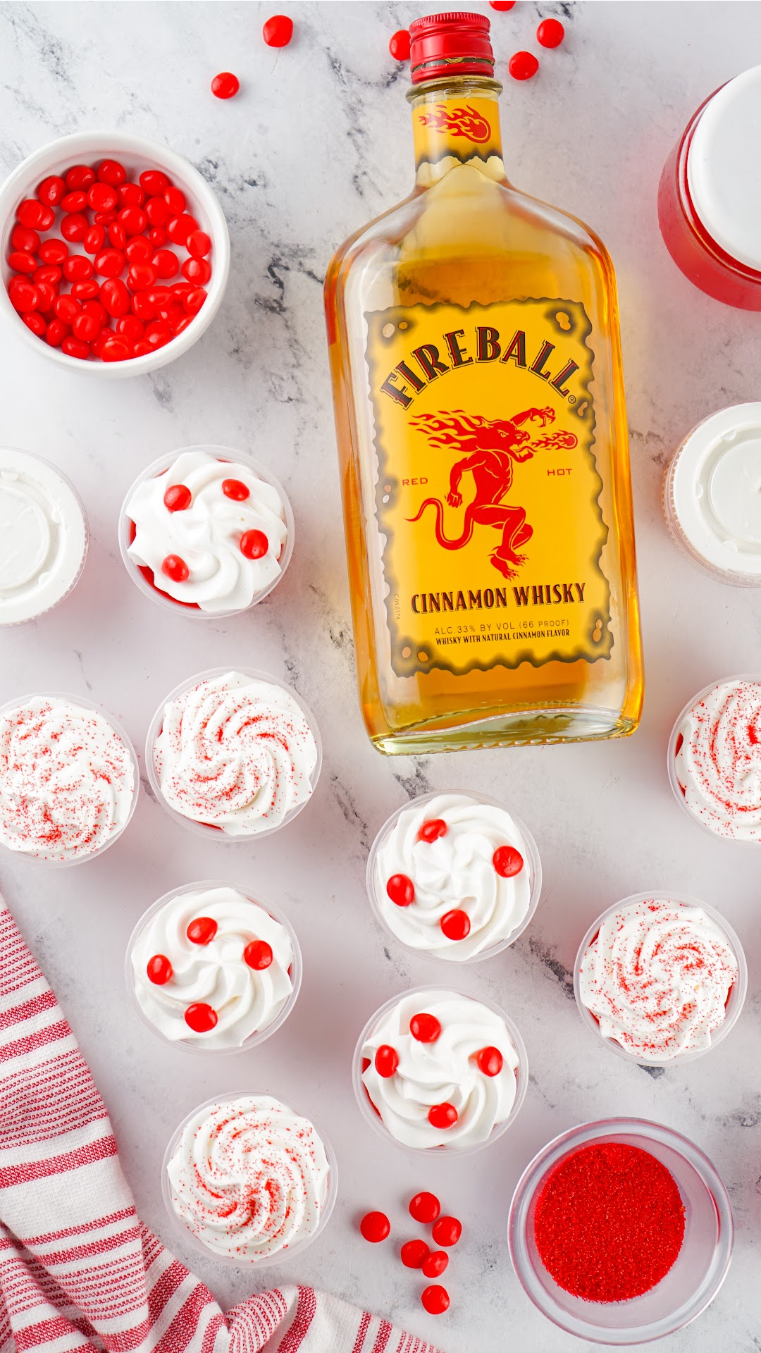 Looking down from above on Red fireball jello shots with a bottle of Fireball. Topped with whipped cream and red hot candy and red sprinkles.