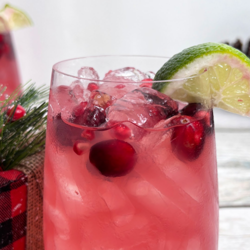 Image of a Christmas margarita with fresh cranberries and a lime wedge as garnish.