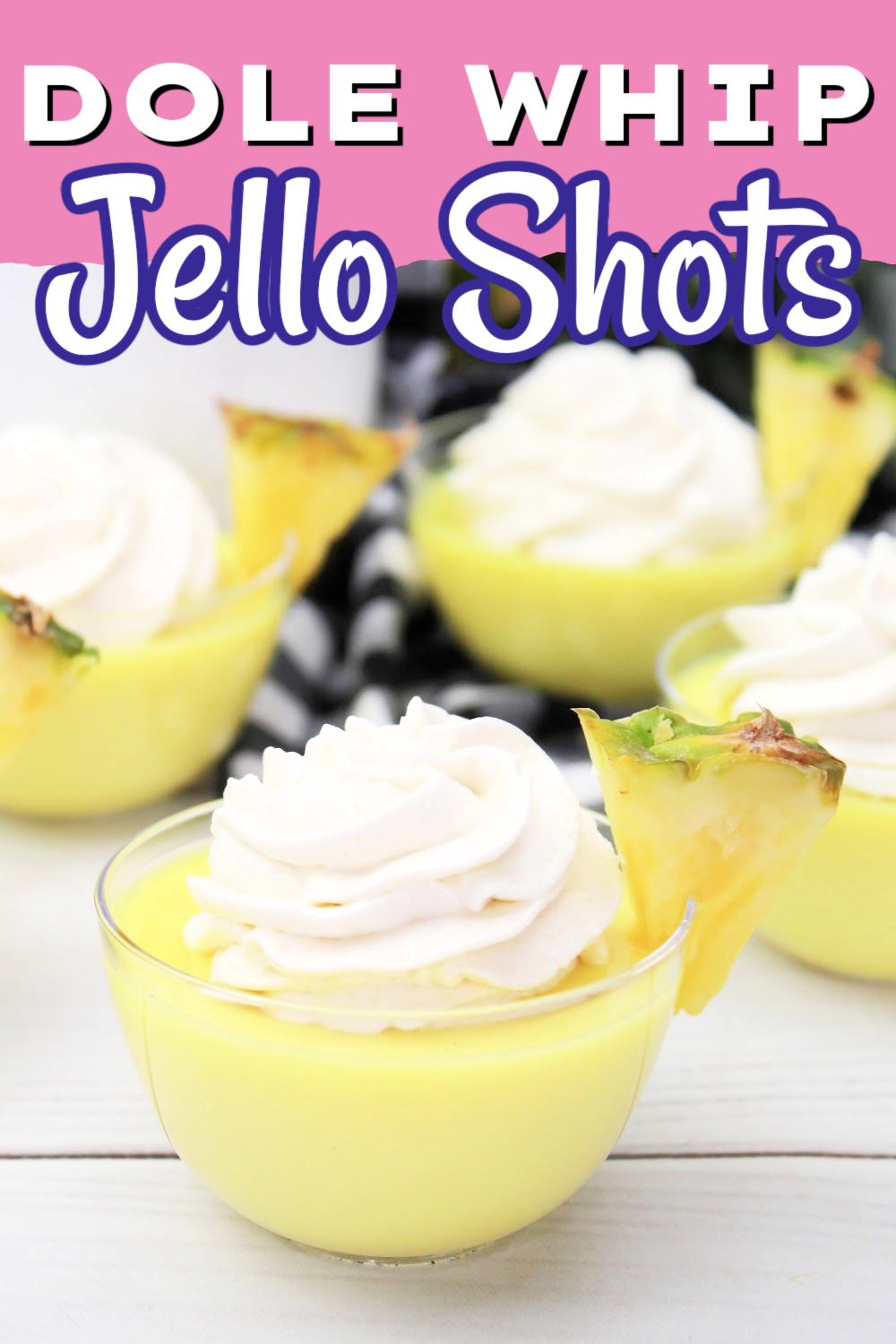 A Dole Whip jello shot in small cups topped with whipped cream and garnished with a small wedge of pineapple.