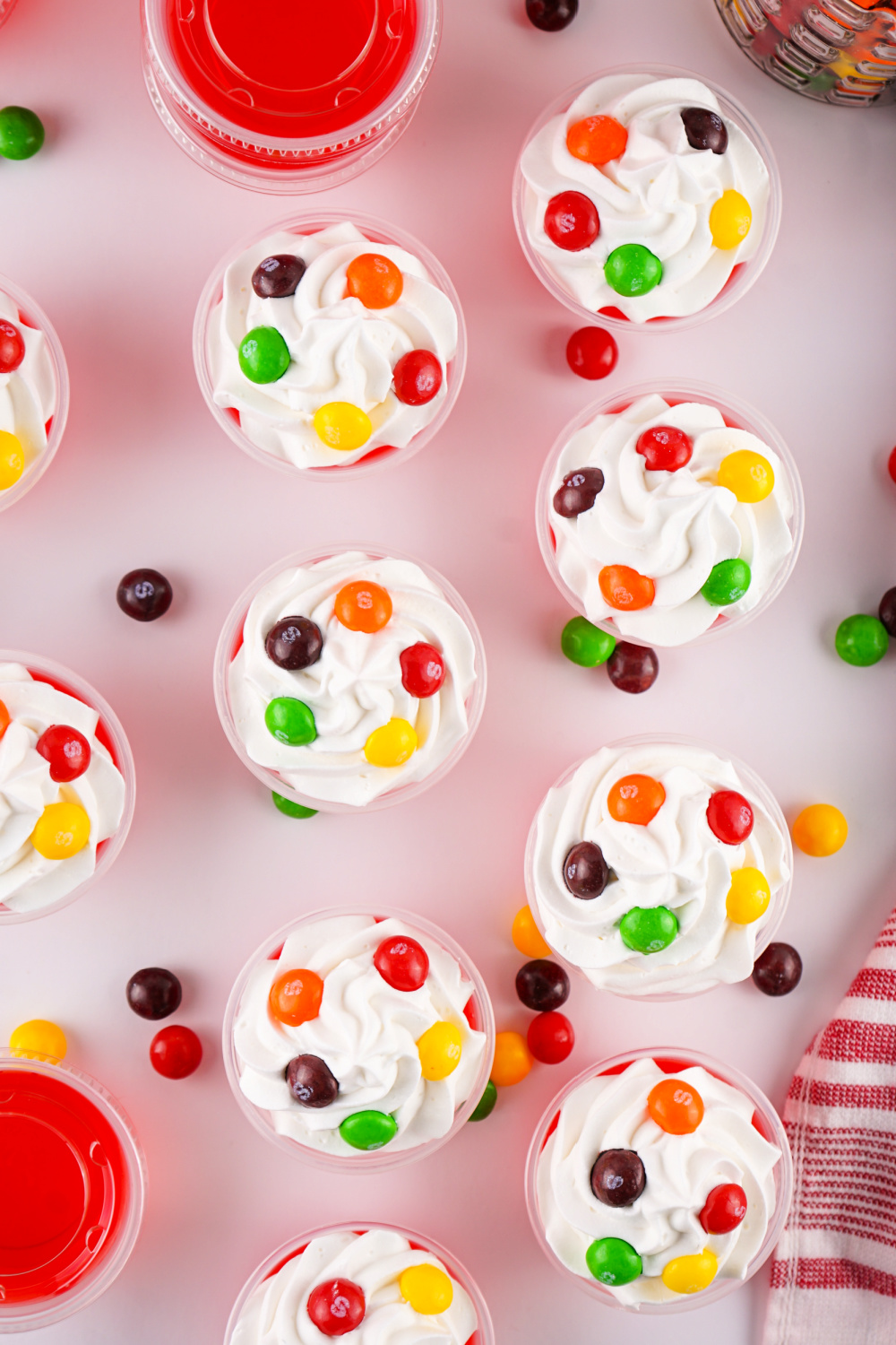 Looking down from above a table with Skittle jello shots topped with whipped cream and Skittle candy.