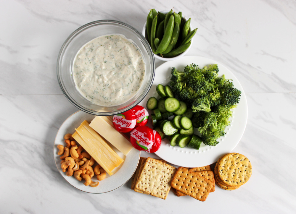 Ingredients for an Easter charcuterie board. Crackers, cheeses, dip, veggies and nuts.