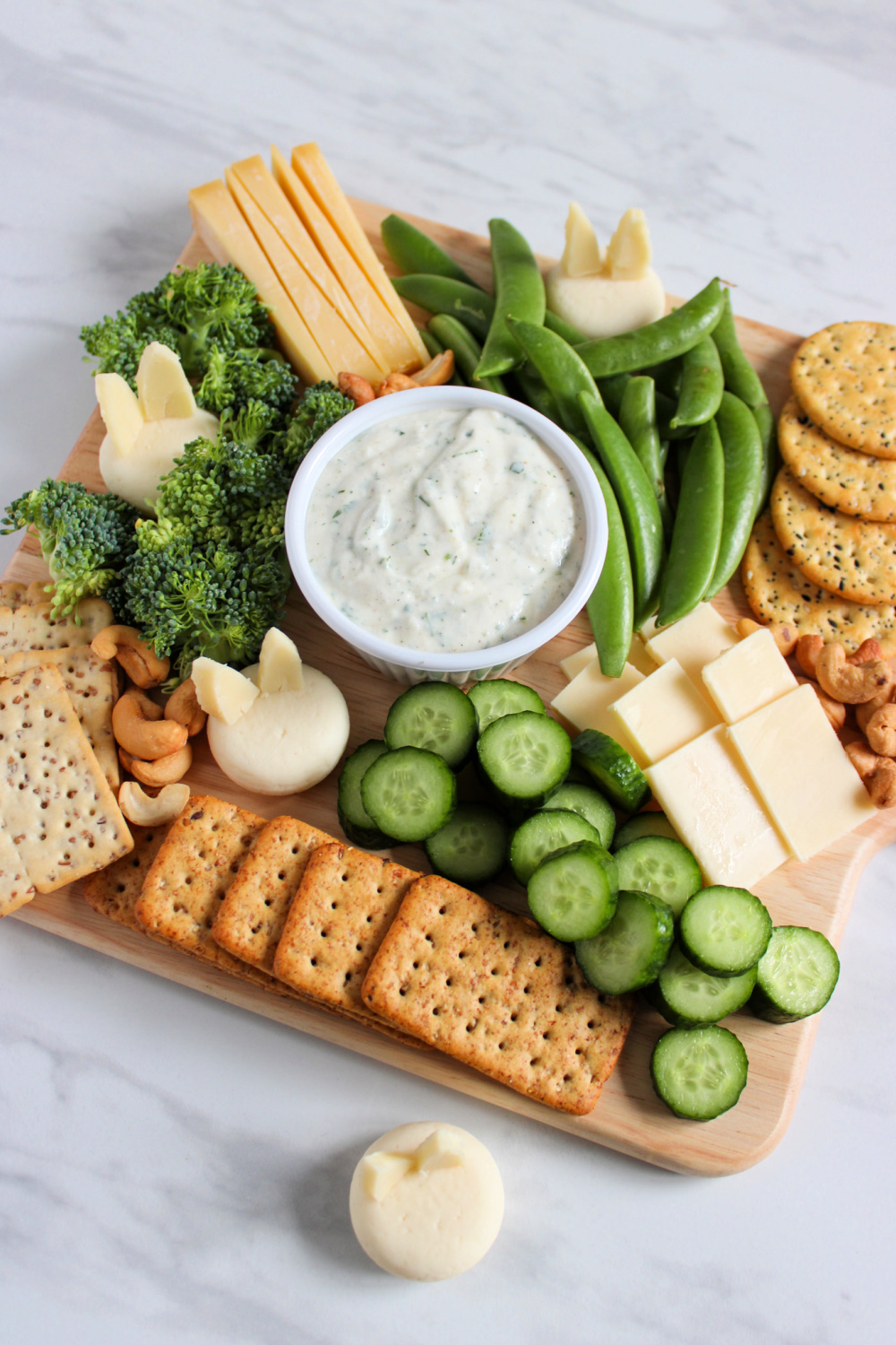 look down on the spring charcuterie board is the dip in the center surrounded by green vegetables, crackers and cheese made to look like bunnies.