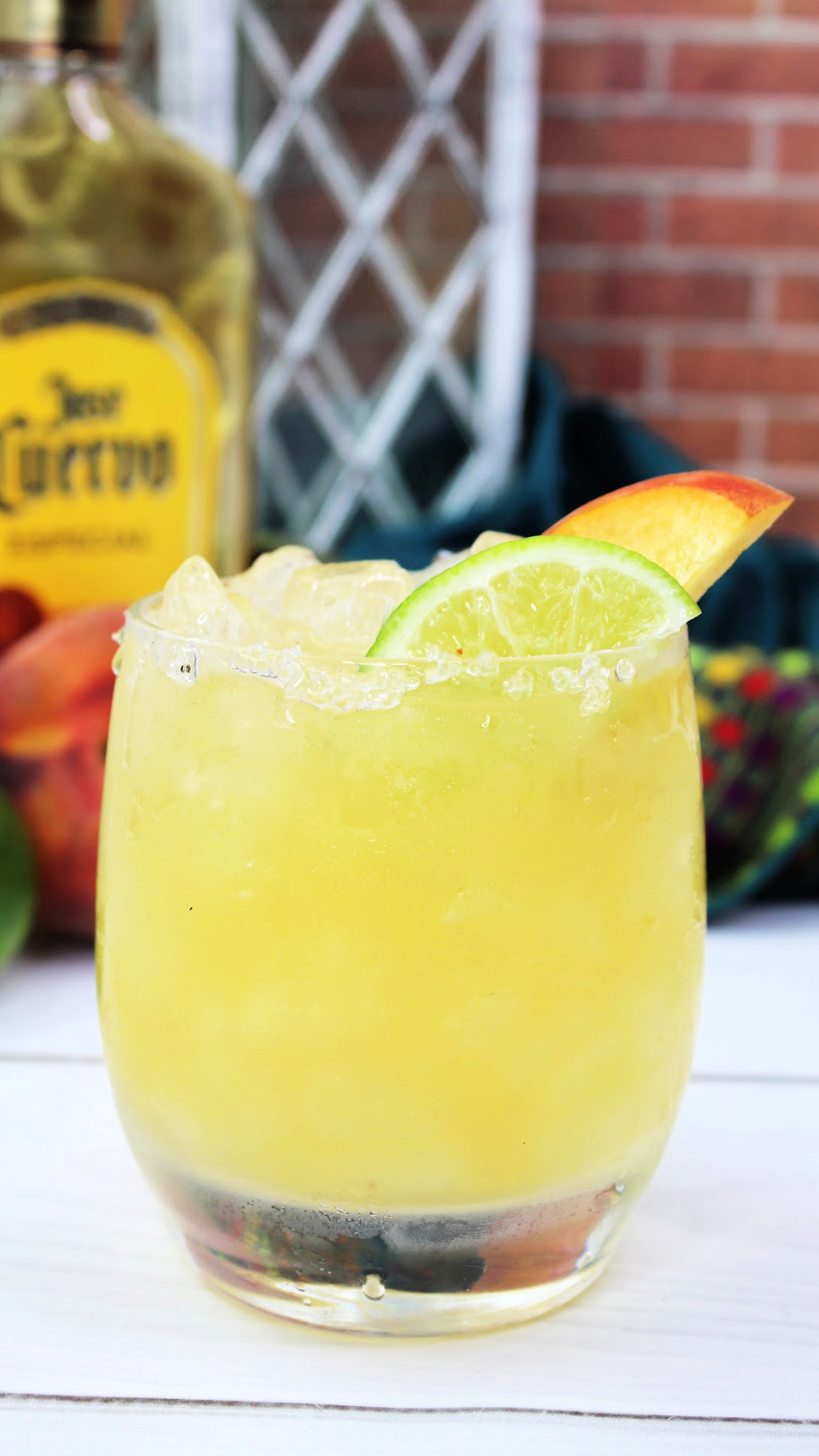 A peach margarita garnished with a slice of peach and a wedge of lime.
