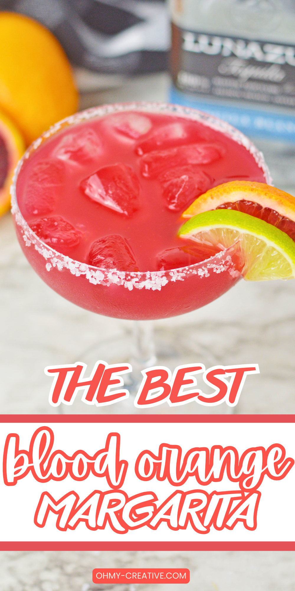 A vibrant glass of blood orange margarita filled with ice and garnished with lime and blood orange slices. The rim of the glass is coated with coarse salt. The text on the image reads 'The Best Blood Orange Margarita' with the website 'ohmy-creative.com' at the bottom.