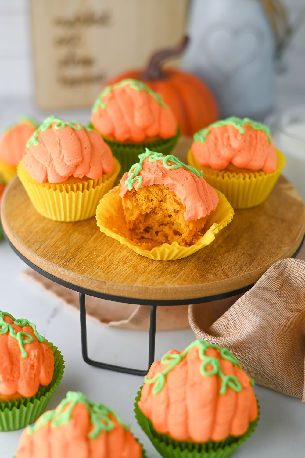 Finished decorated pumpkin cupcakes on a teared wood tray. A bite is taken out of one of the cupcakes.