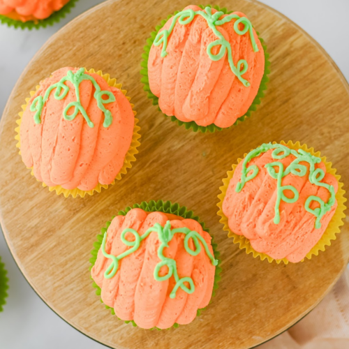 A closeup of pumpkin decorated cupcakes for fall on a wood tray.