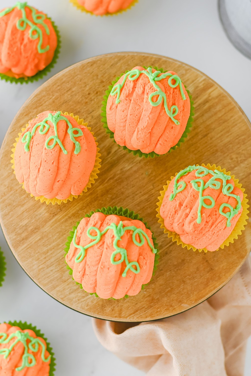 A closeup of pumpkin decorated cupcakes for fall on a wood tray.