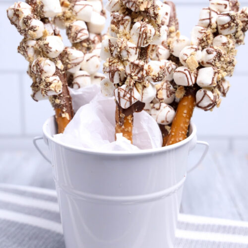 A white container with s'mores pretzel rods with a gray napkin on the table.