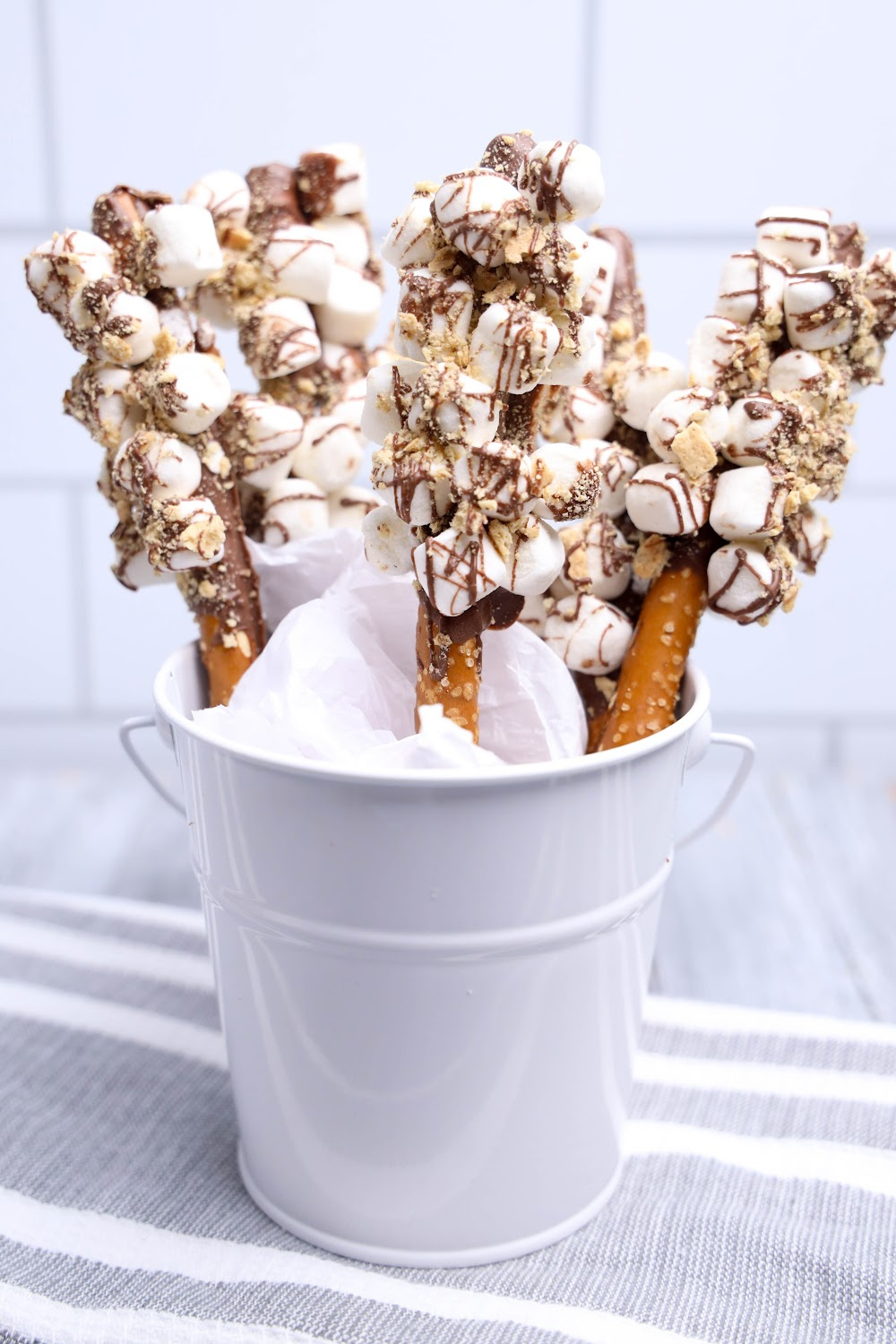 A white container with s'mores pretzel rods with a gray napkin on the table.